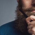 Handsome young man styling his beard with a comb