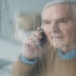 Behind the rainy glass view of senior disturbed man making a phone call