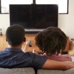 Rear View Of Couple Sitting On Sofa Watching TV Together