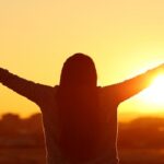 Backlight of a woman raising arms with thumbs up